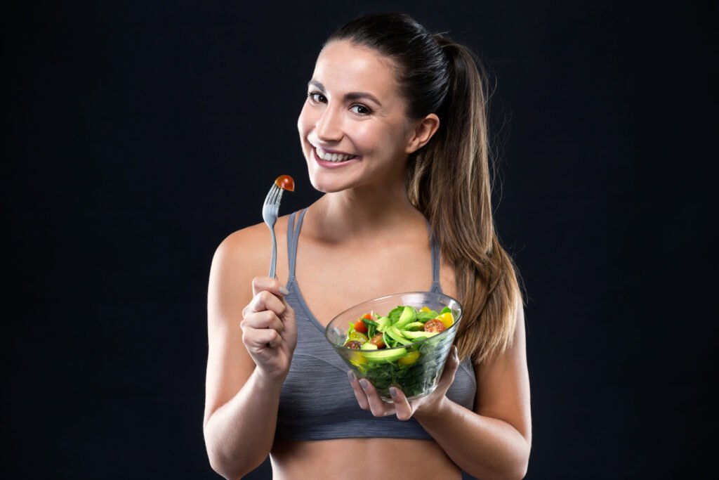 beautiful young woman eating salad black background