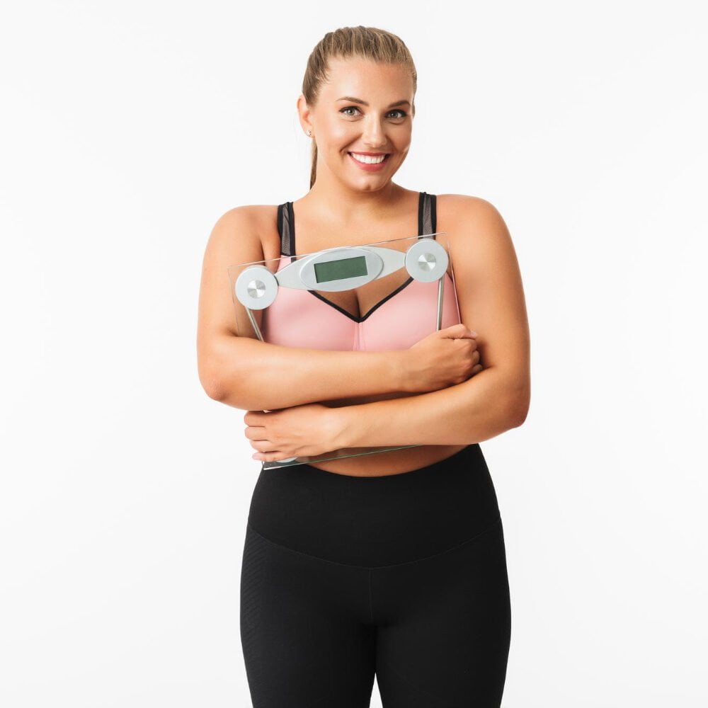 Young Smiling Woman With Excess Weight Sporty Top Holding Scales Hands While Happily Looking Camera White Background